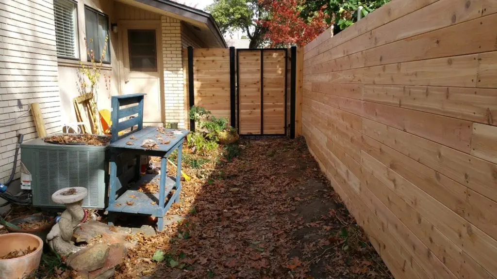 A house and sideyard with horizontal cedar wood fence and gate with black steel frame