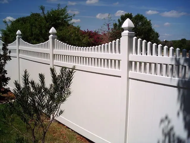 White picket vinyl fence against a pine tree in the backgrounndn