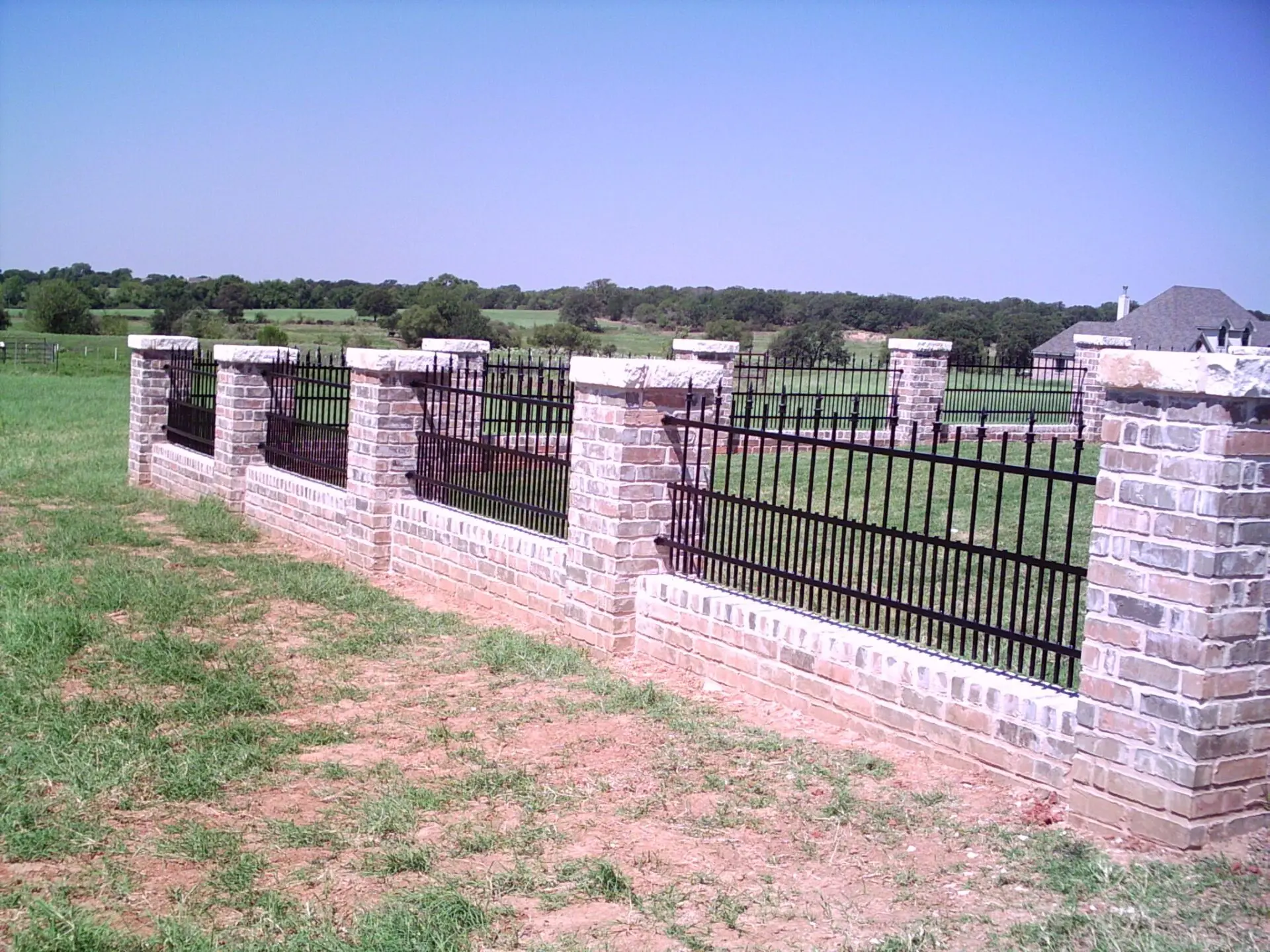 A fenced area by a black iron fence with brick pillars